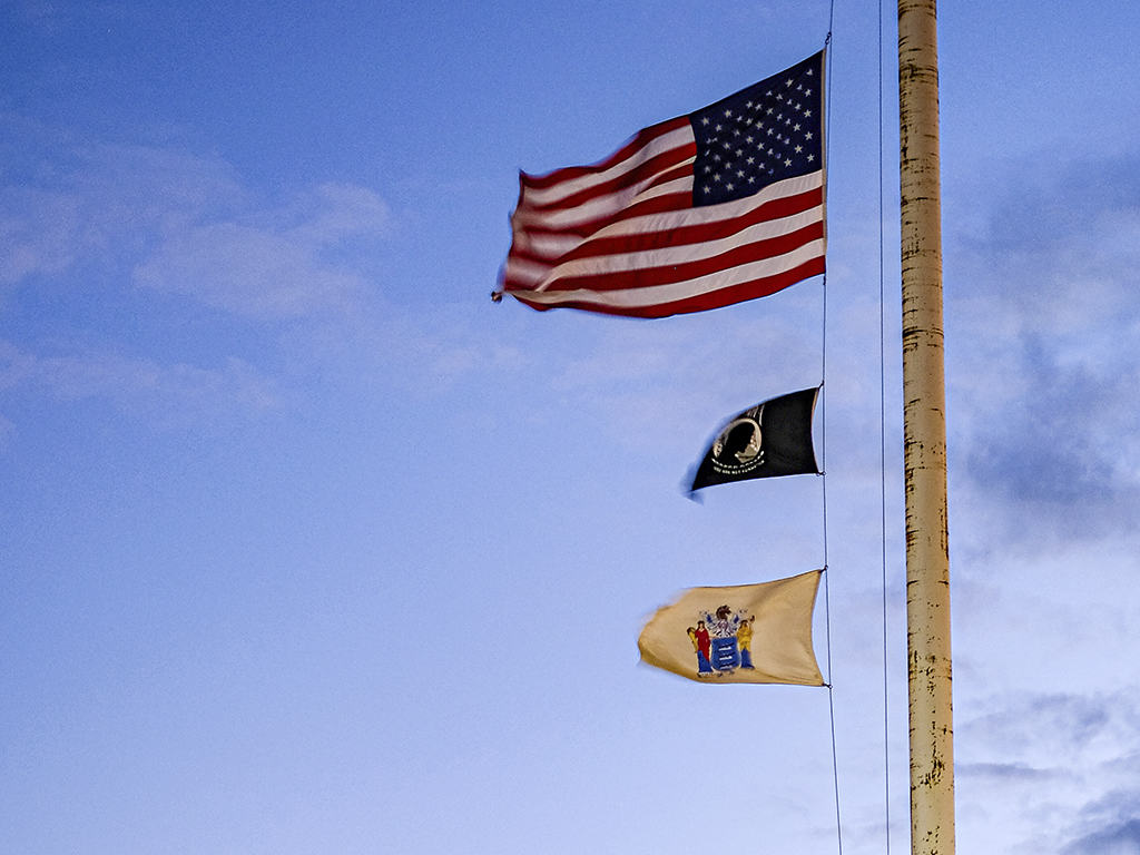 Three flags on a flagpole: the United States flag, a prisinor-ow-war missing-in-action flag, and the State of New Jersey flag